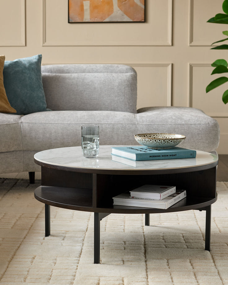 Aurora round coffee table with white marble top and black oak base, featuring open shelf storage, styled in modern living room.