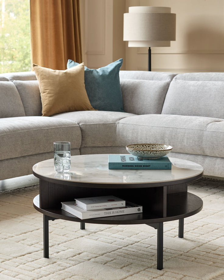 Aurora round coffee table with white marble top and dark oak base, featuring open shelf storage, styled in a modern living room.
