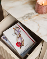 Austin bedside table in natural ceramic finish, styled with books, glasses, and a lit candle on marble top.