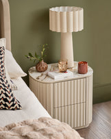 Austin bedside table in natural ceramic with vertical ribbed front, marble top, and two drawers, styled in a bedroom setting.