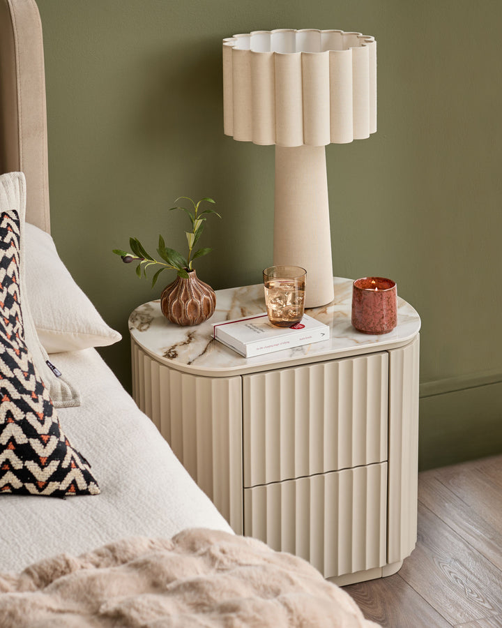 Austin bedside table in natural ceramic with vertical ribbed front, marble top, and two drawers, styled in a bedroom setting.