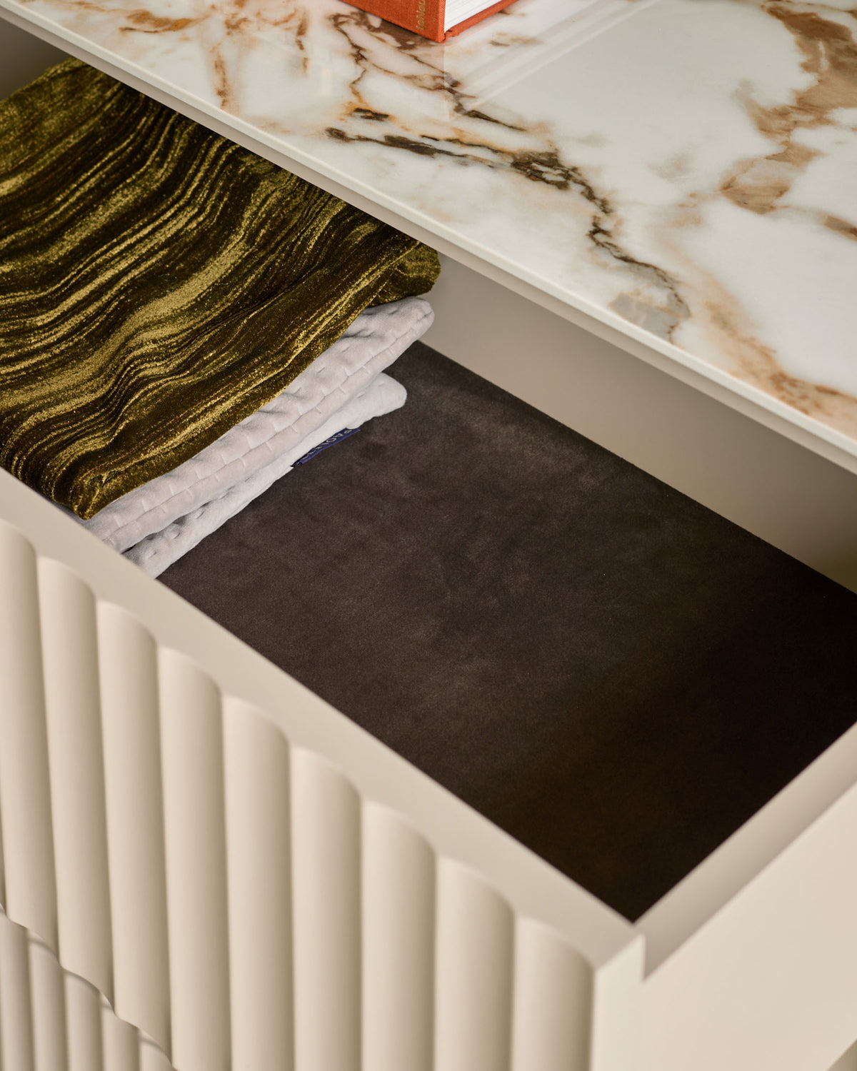 Austin chest of drawers in cream with open drawer displaying black interior and folded olive and white linens on top.