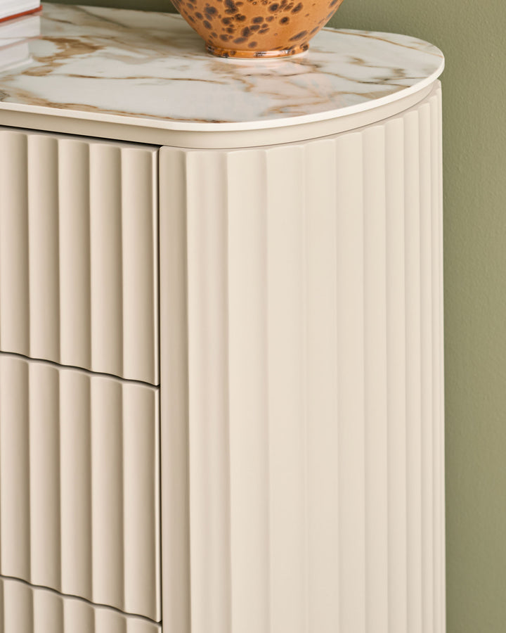 Austin chest of drawers in natural ceramic with marble-look top and fluted front panels, shown at an angle.