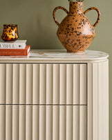 Austin chest of drawers in natural ceramic with vertical fluted detailing and rounded marble top, styled with decorative objects.