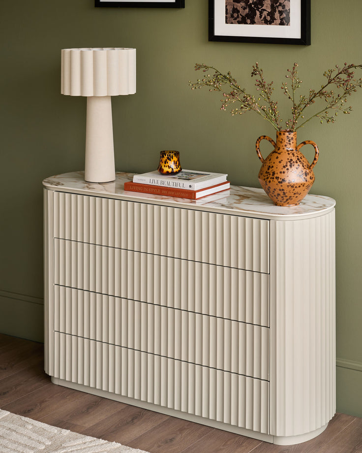 Austin chest of drawers in cream with fluted ribbed texture, marble top, and four drawers styled with lamp and decorative objects.