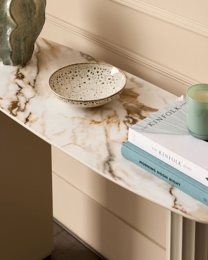 Austin console table in natural marble with speckled ceramic bowl, stacked books, and green candle displayed on top.