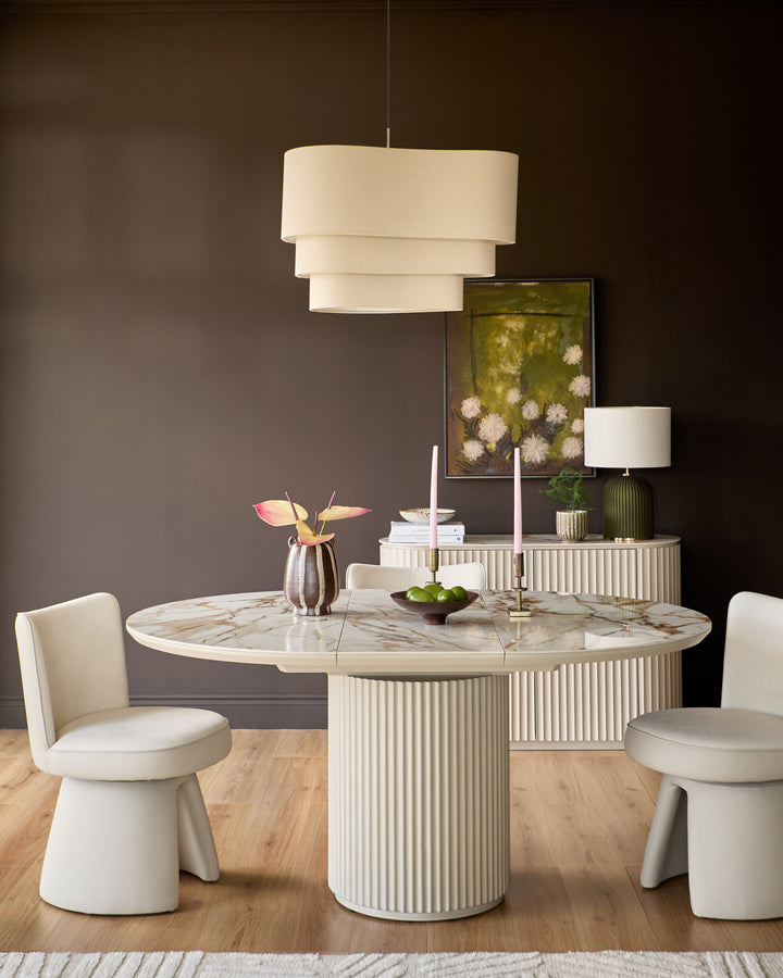 Austin extending dining table in natural ceramic with ribbed white base, round marble top, styled with cream chairs and pendant light.