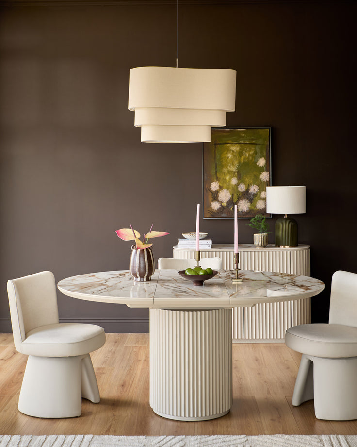 Austin extending dining table in natural ceramic with ribbed white base, round marble top, styled with cream chairs and pendant light.