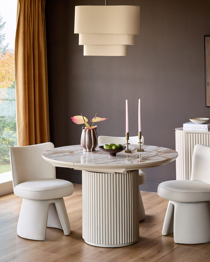 Cream swivel dining chair with curved backrest, shown in modern dining room setting with round marble table and pendant light.