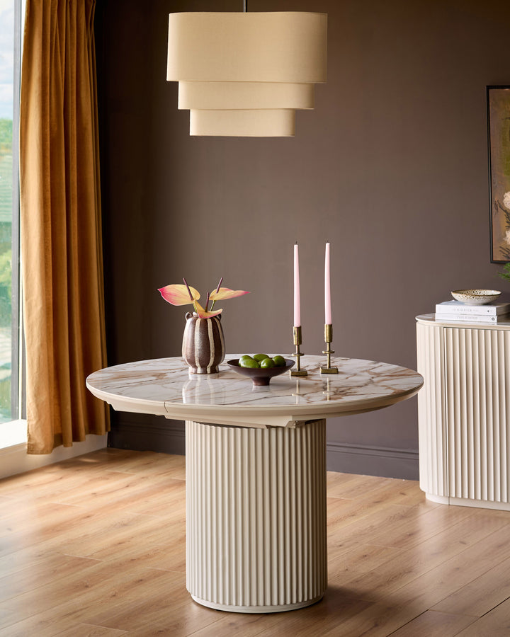 Austin extending dining table in natural ceramic with fluted cream base, round marble top, styled with candlesticks and flowers.