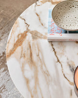Close-up of a white, marble-effect round coffee table with a bowl, book and candle on top, ideal for a modern living room.