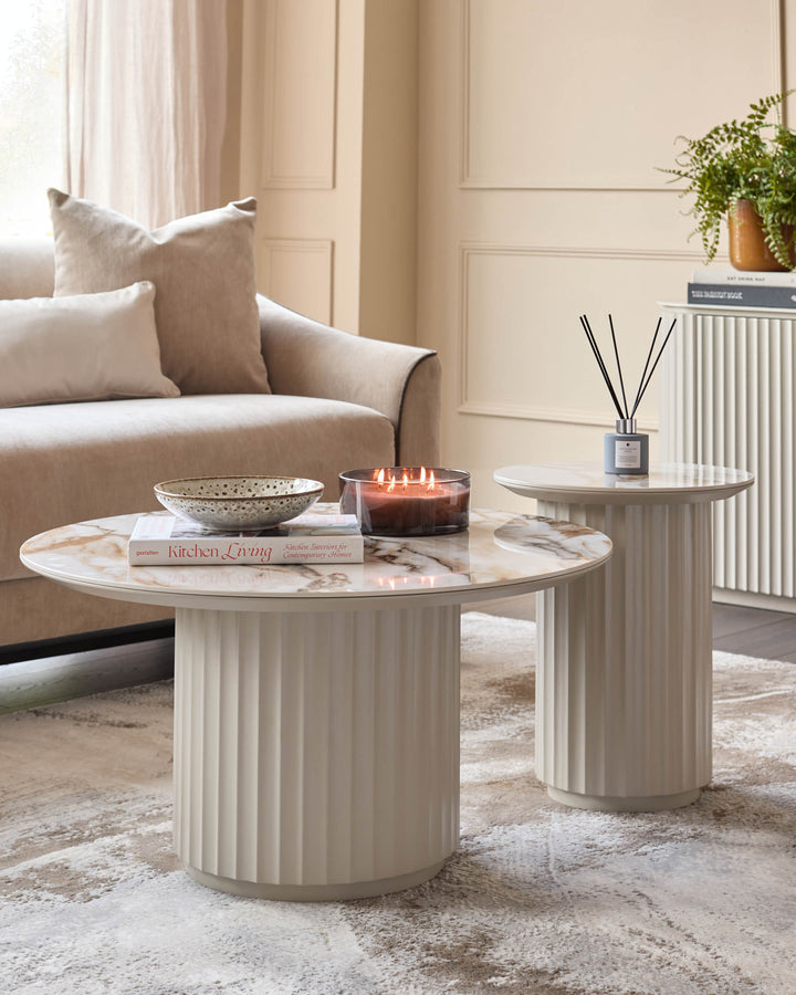 Two neutral coloured coffee tables with marble effect tops. A sofa and side unit are behind the tables.