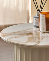 A stylish round coffee table with a marble effect top, accompanied by a reed diffuser and candle, creating a cosy atmosphere.