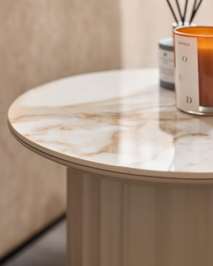 A close up of a round side table in a neutral colour palette with a marble effect top and various accessories.