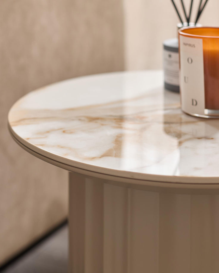 A close up of a round side table in a neutral colour palette with a marble effect top and various accessories.