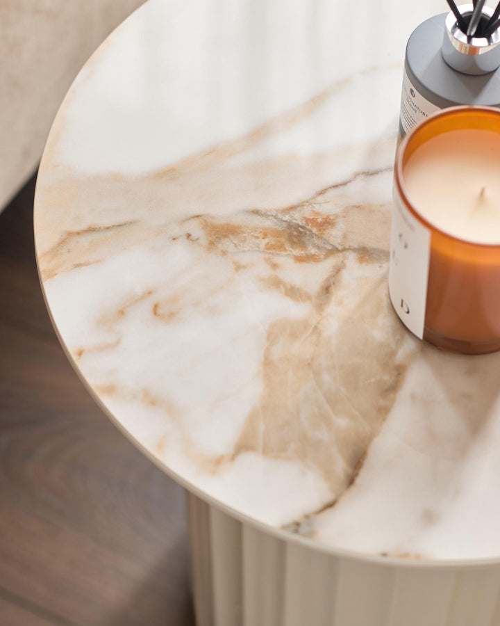 A stylish round marble side table with a ribbed base, featuring a candle and reed diffuser. Modern and chic.