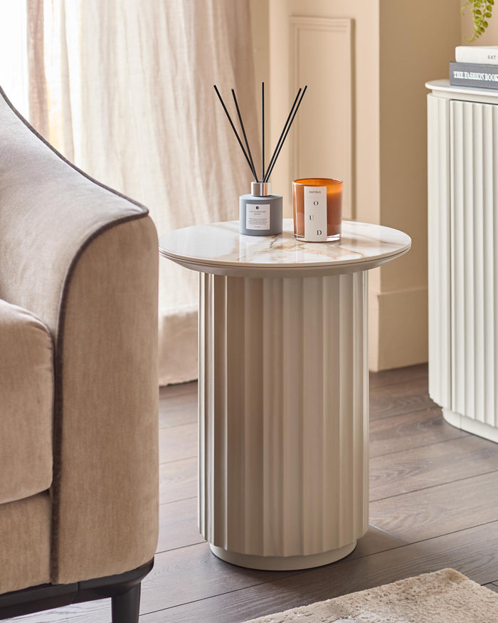 A stylish side table with candles and fragrance sticks, next to an elegant neutral armchair and a white sideboard.
