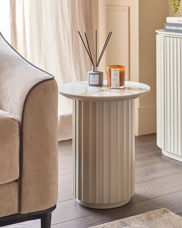 A stylish side table with candles and fragrance sticks, next to an elegant neutral armchair and a white sideboard.
