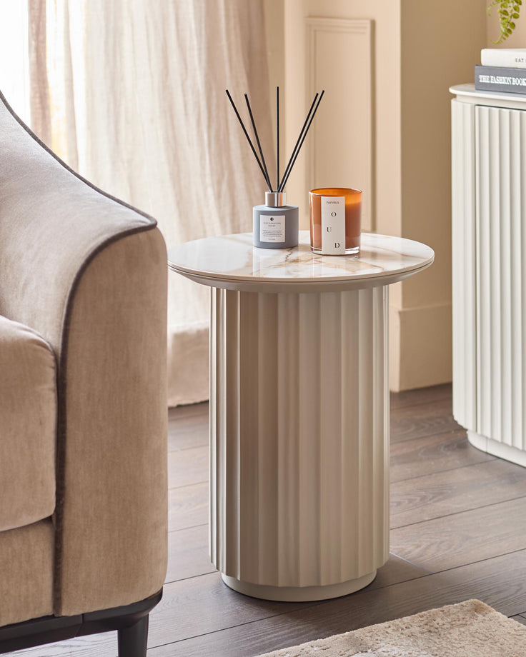 A stylish side table with candles and fragrance sticks, next to an elegant neutral armchair and a white sideboard.