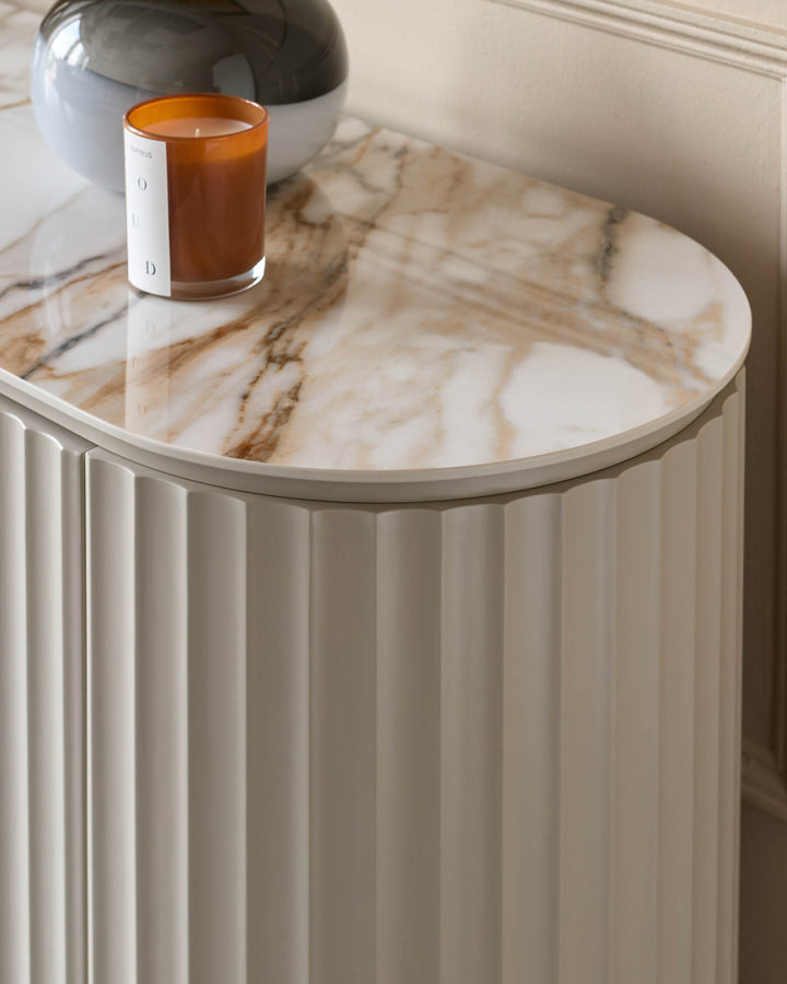 Elegant side table with a marble top and ridged cabinet, paired with a stylish glass vase and scented candle.