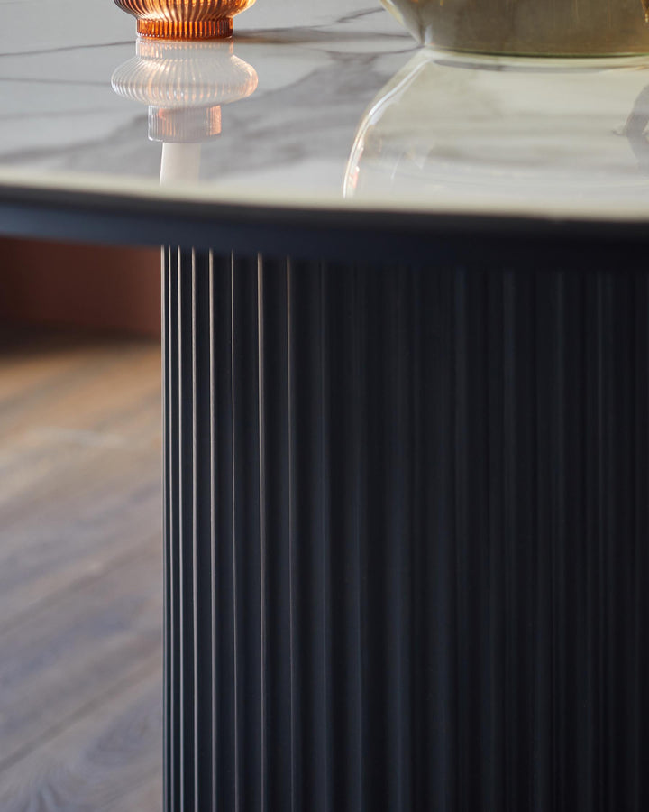 Close up of a round marble-topped table with a ribbed, cylindrical base, and amber glass decorative objects on top.