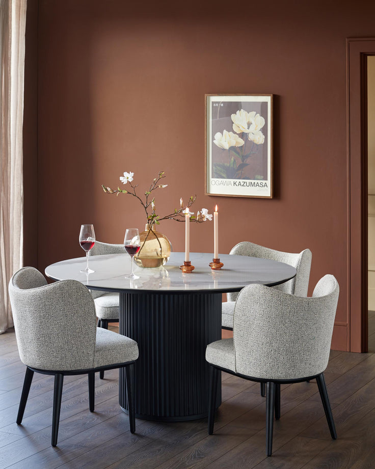 A dining set featuring a round table with grey upholstered chairs, perfect for a modern dining space.