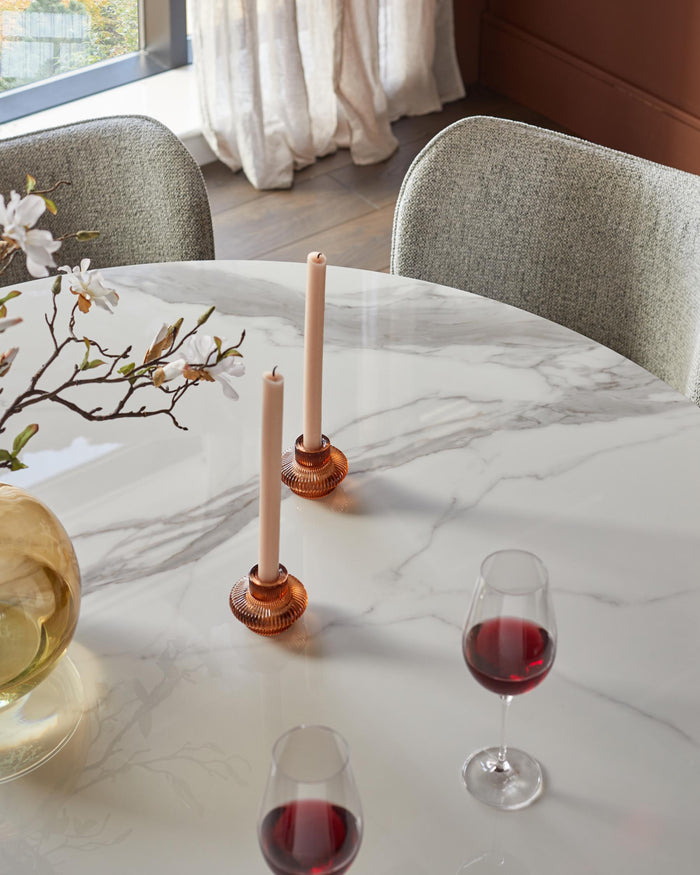 A stylish dining arrangement featuring a marble-effect table, upholstered chairs, candles and wine glasses.