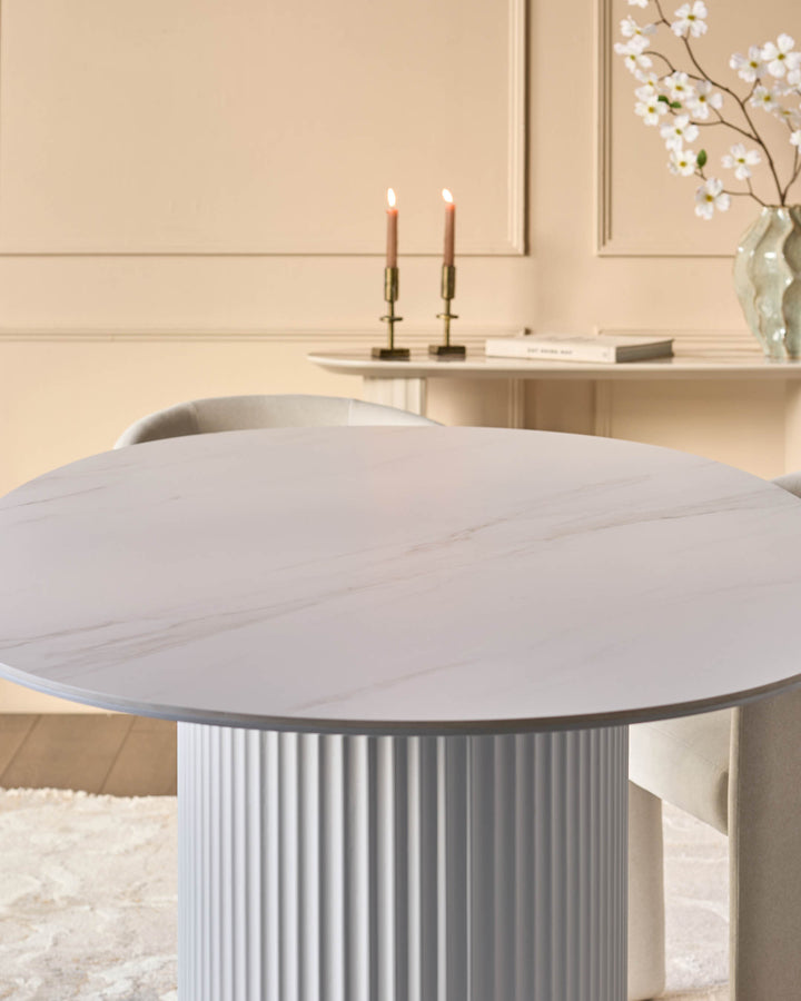 Austin ceramic fluted dining table in white with round top and ribbed pedestal base in a minimalist bedroom setting.
