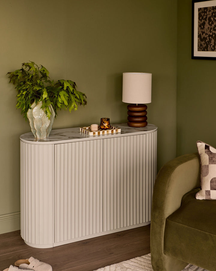 Austin Compact Sideboard in natural ceramic with vertical ribbed detailing, marble top, displayed in a styled living room setting.