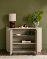 Austin Compact Sideboard in natural ceramic finish with ribbed vertical detailing, open doors, and internal shelving displayed against sage green wall.