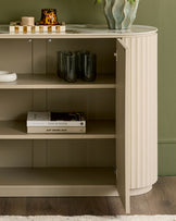 Austin compact sideboard in natural ceramic finish, curved design with open shelving displaying glassware and books.