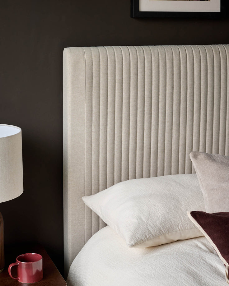 Cream fabric king-size bed with vertical channel tufting on headboard, styled with white bedding and burgundy accents.