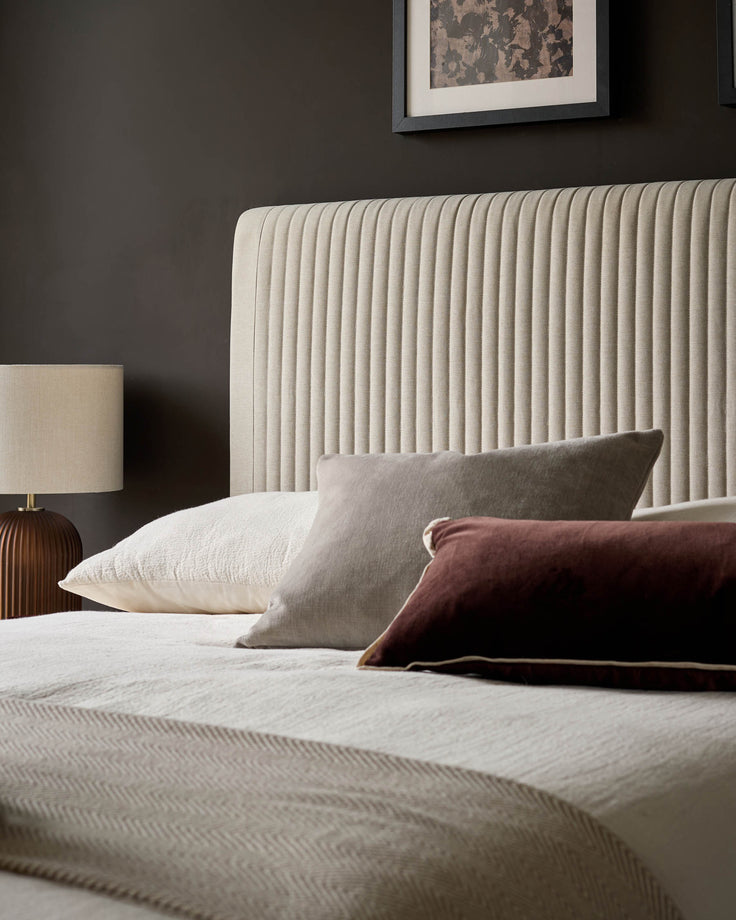 Cream fabric king-size bed with vertical ribbed headboard, styled with pillows and bedding in a modern bedroom setting.