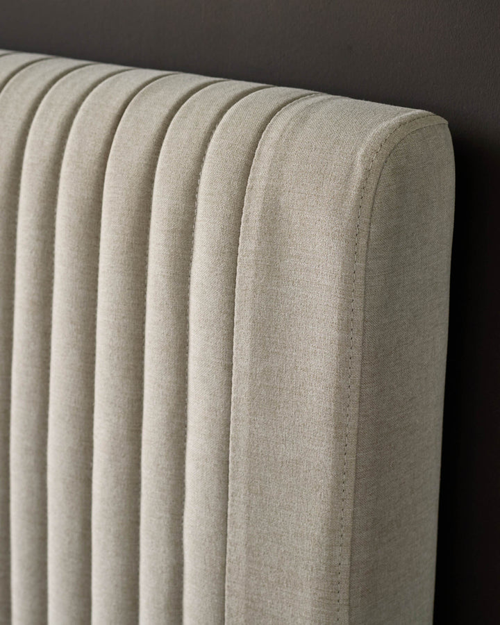 Cream fabric king-size bed headboard with vertical ribbed quilting detail, close-up side view.