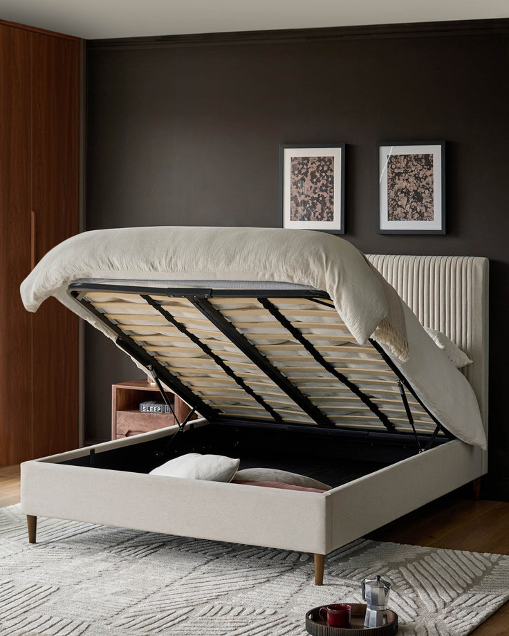 Cream fabric king-size bed with storage, featuring an open lift-up base revealing wooden slats and storage space underneath.