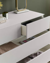 Modern white chest of drawers with open drawers, revealing magazines and clothing.