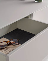 Open white drawer with tortoiseshell glasses and a notebook inside, showcasing modern bedroom furniture.