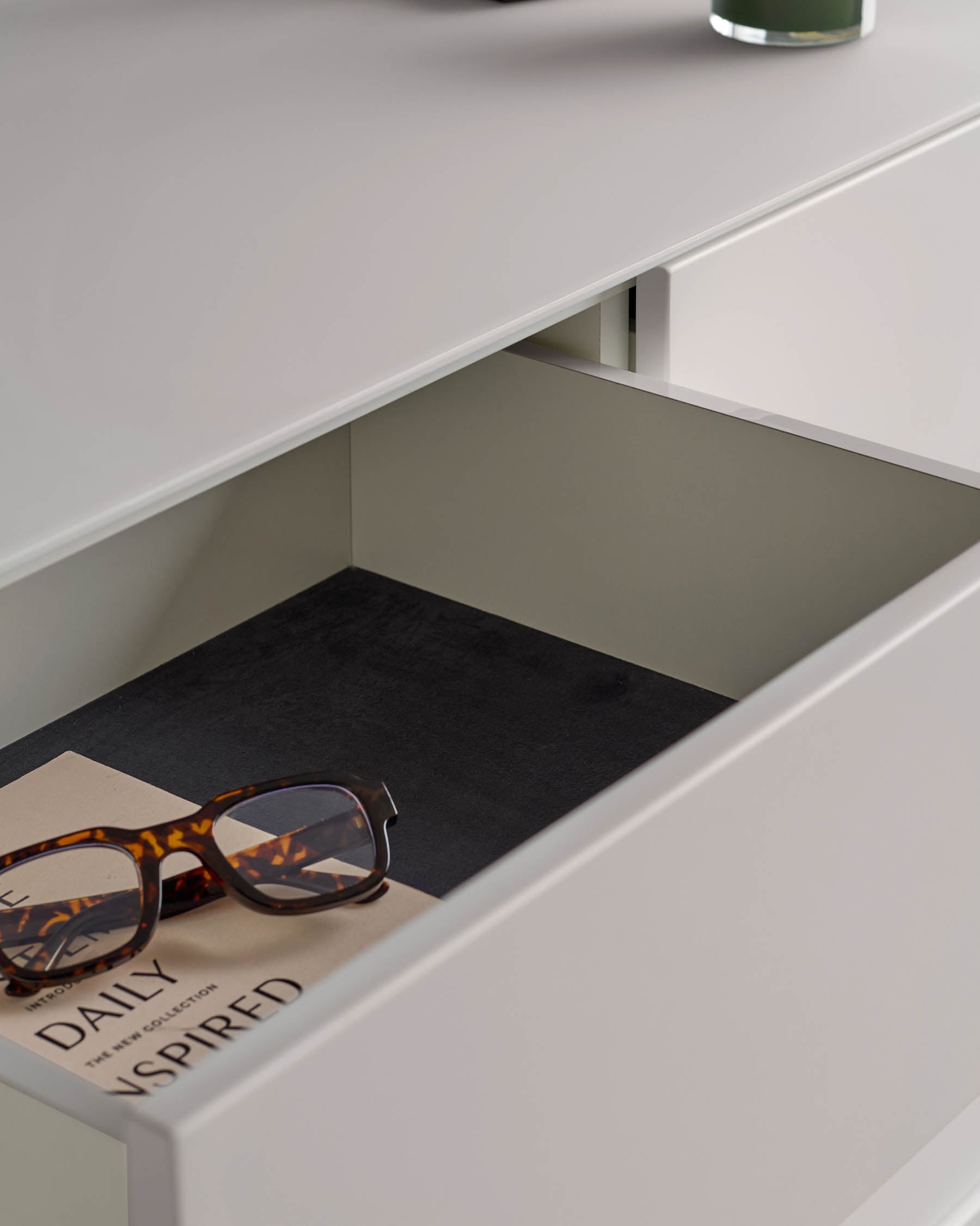 Open white drawer with tortoiseshell glasses and a notebook inside, showcasing modern bedroom furniture.