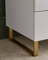 Close-up of white cabinet with gold legs. The cabinet has drawers and is on a wood floor.