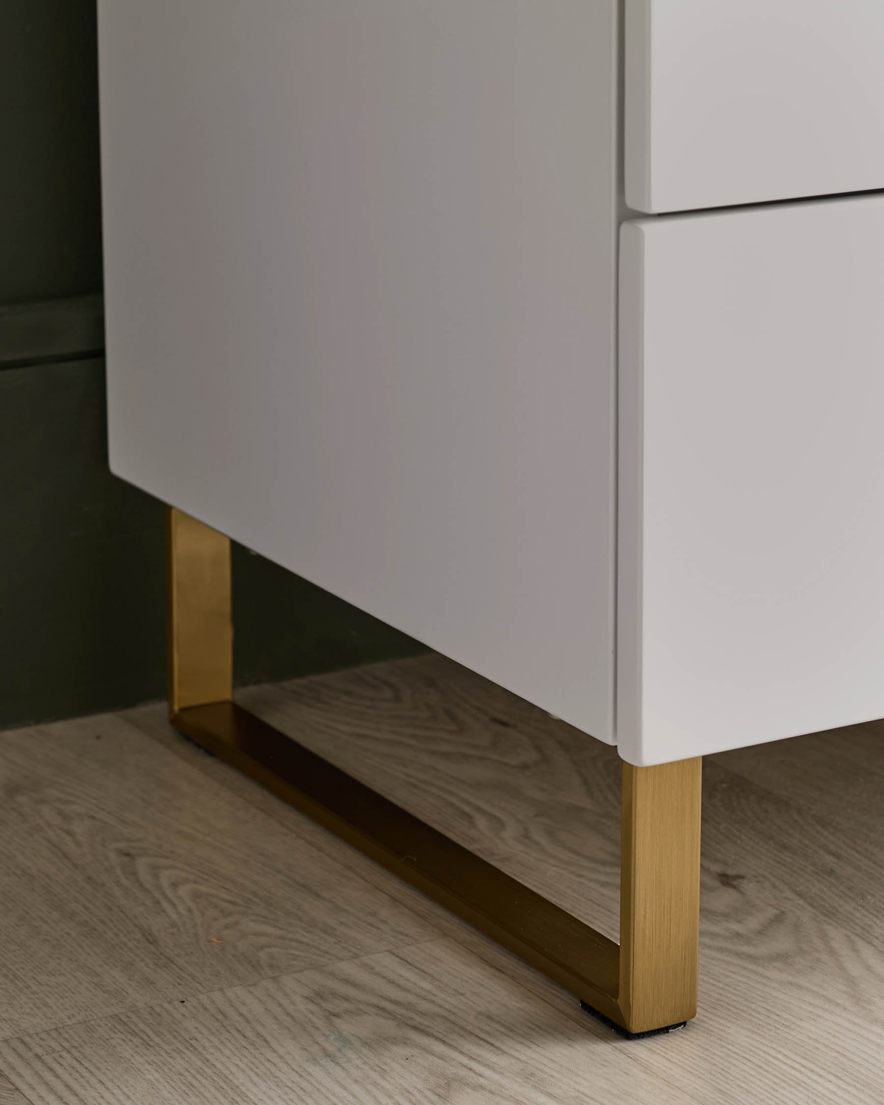 Close-up of white cabinet with gold legs. The cabinet has drawers and is on a wood floor.