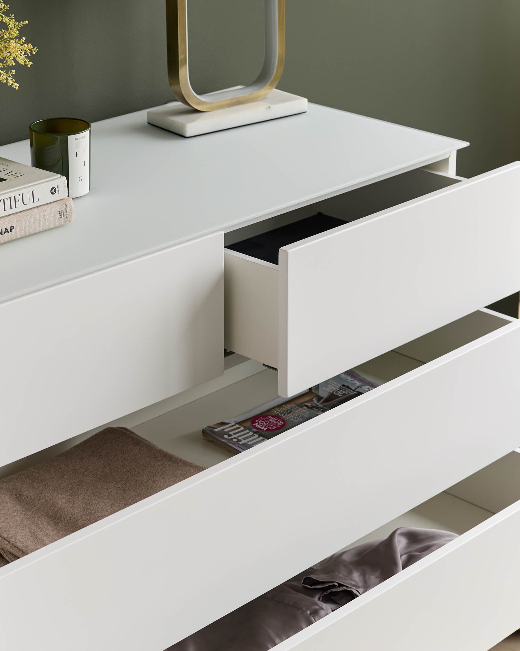 A minimalist white chest of drawers with open drawers, revealing neatly folded items. A stylish storage solution.