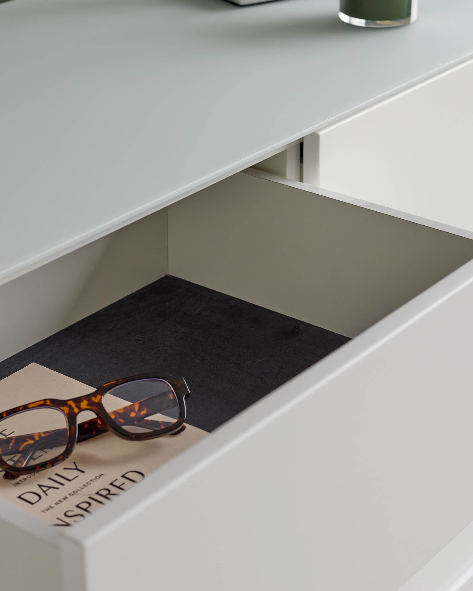 A white drawer containing a book and tortoise shell framed glasses.