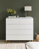 White chest of drawers with gold legs, styled with a lamp, flowers, books and candle.