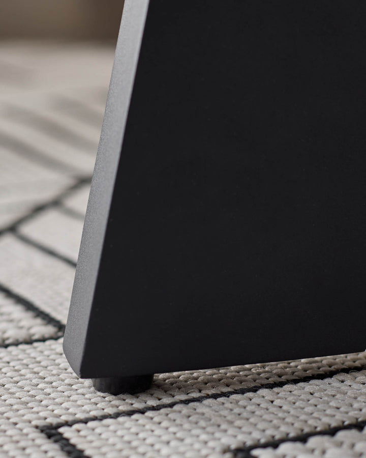 Black garden side table base detail on woven outdoor rug, close-up of leg and textured surface.