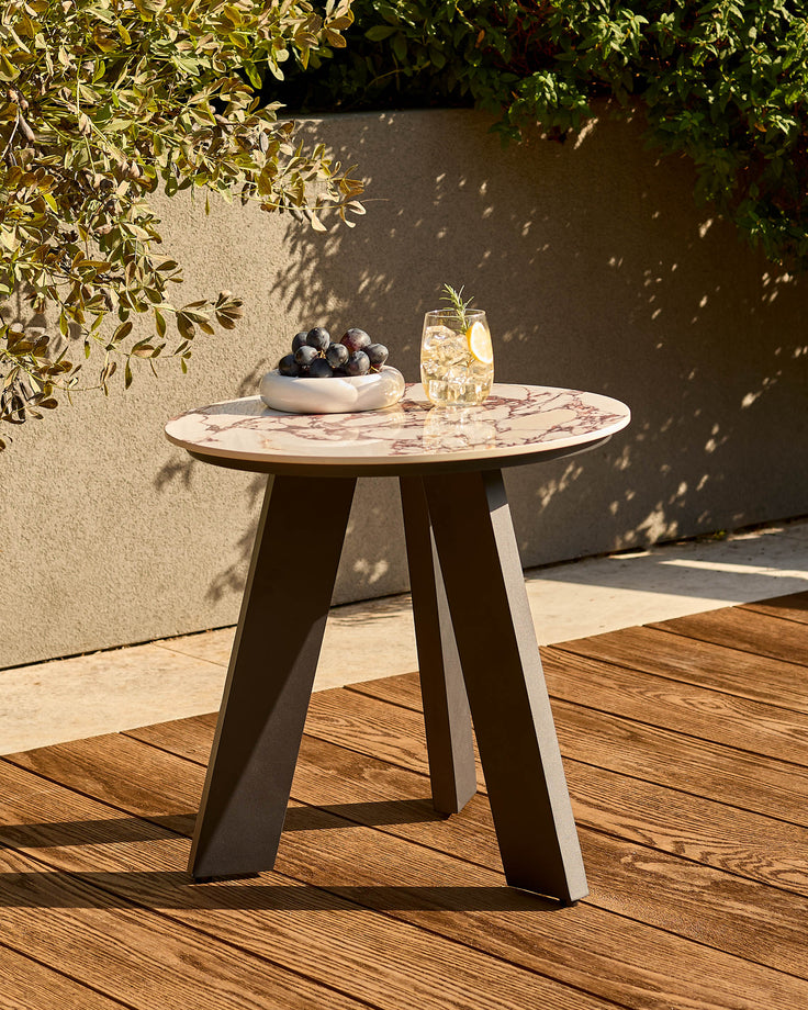 Bianco garden side table with black base and white Calacatta marble top, styled outdoors on wooden deck with grapes and drink.