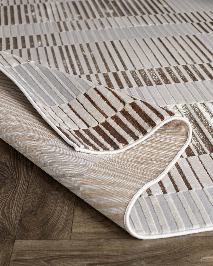 A striped rug with brown and beige tones is partially folded on a wood floor. The rug's edges are bound in white.