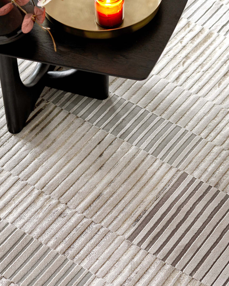Elegant round coffee table with a glossy dark finish and robust cylindrical legs, partially visible on a textured striped area rug with shades of grey and beige.