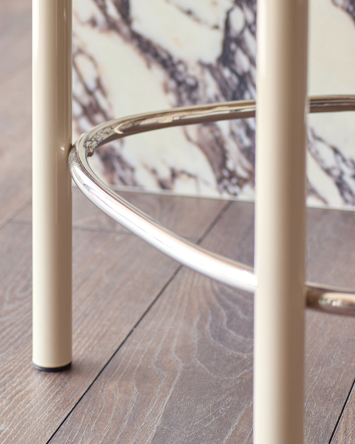 Blake bar stool in champagne velvet with chrome footrest and cream legs, shown from side angle on wooden floor.