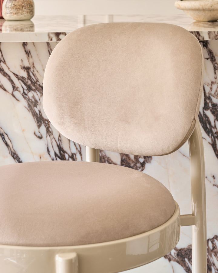 Blake bar stool in champagne velvet with rounded backrest, shown from side angle against marble backdrop.