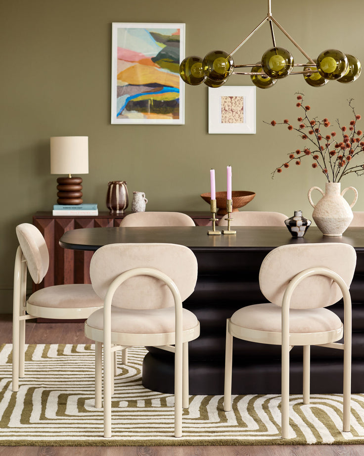 Blake dining chair in champagne velvet with curved backrest and cream-colored frame, shown in dining room setting.